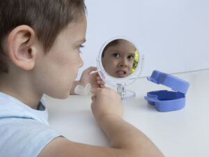 Boy looking into a mirror as he places his orthodontic device into his mouth to correct a misalignment.